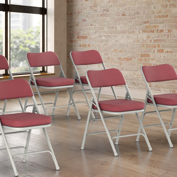 A group of Lancaster Table & Seating burgundy fabric folding chairs with red cushions.