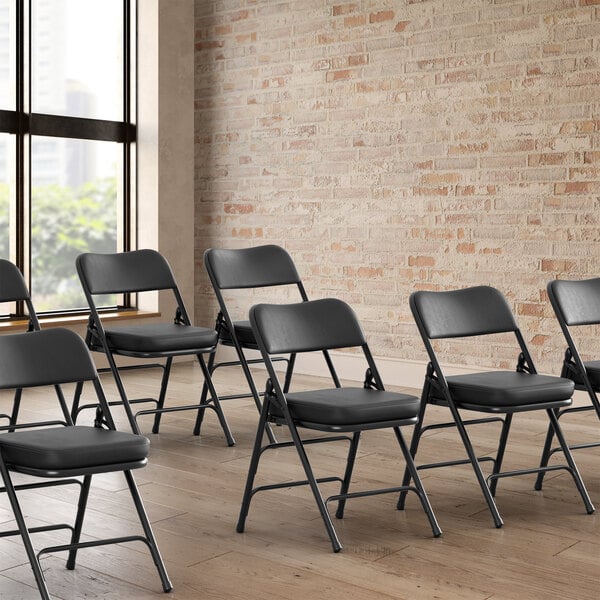 A row of Lancaster Table & Seating black folding chairs with black padded seats.