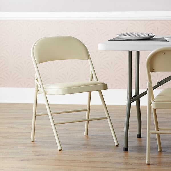 A beige Lancaster Table & Seating folding chair with a padded seat.