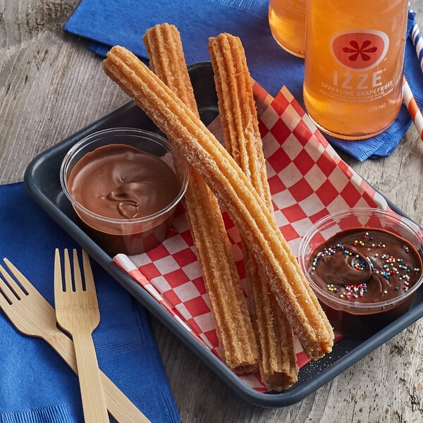 J & J Snack Foods Hola Churros filled with cajeta on a tray with churros and chocolate sauce with wooden forks.