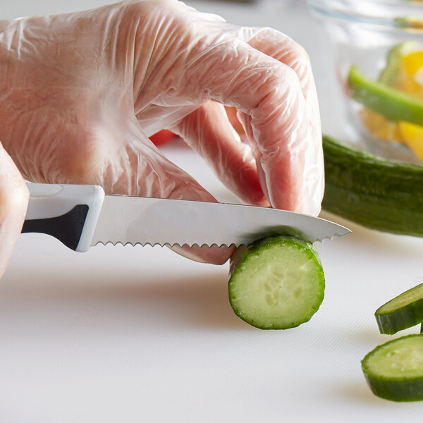 A person in gloves using a Mercer Culinary Millennia serrated paring knife to cut a cucumber.