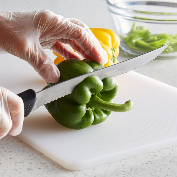 A person in gloves using a Mercer Culinary Millennia wavy utility knife to cut a green bell pepper on a cutting board.