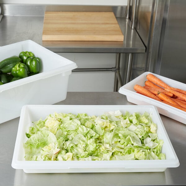 A white Rubbermaid food storage box on a kitchen counter filled with lettuce, carrots, green peppers, and cabbage.