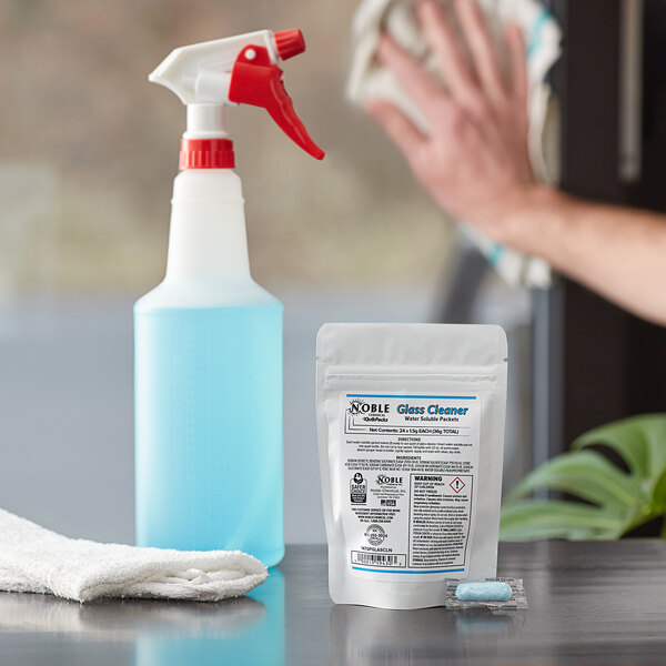 A hand using a Noble Chemical QuikPacks glass cleaner sprayer on a bottle of liquid.