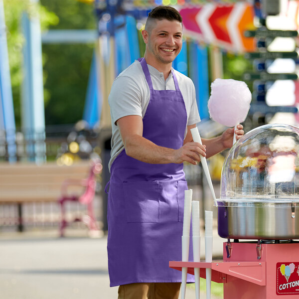 A man wearing a bright purple Choice apron smiling at the camera while making cotton candy.