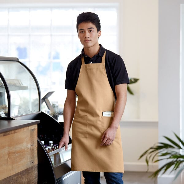 A man wearing a khaki Choice standard bib apron standing in a cafe.