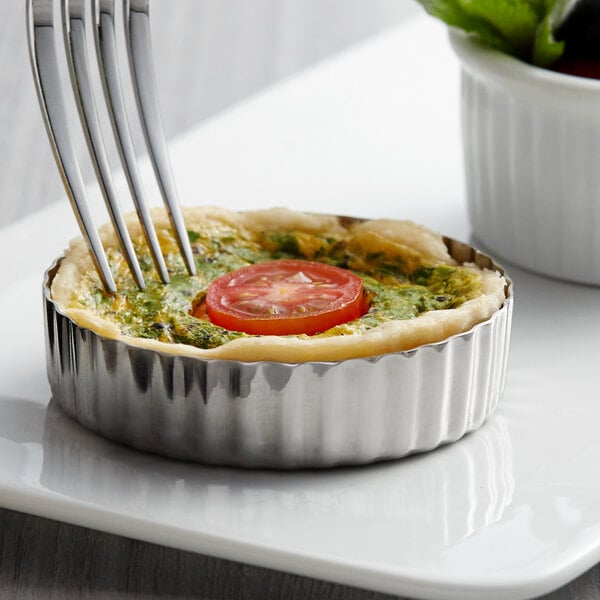 A fork picking up a tomato in a small Vollrath stainless steel round tart.