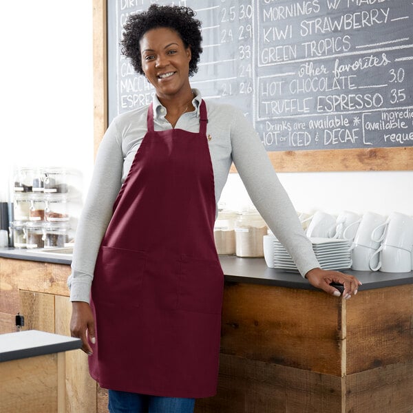 A smiling woman wearing a burgundy Choice bib apron stands in front of a counter.