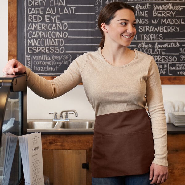 A woman standing at a counter wearing a brown Choice standard waist apron.