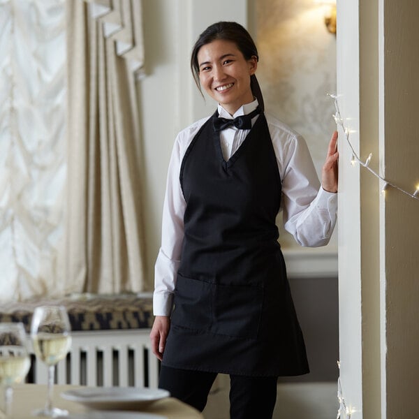 A woman wearing a Choice black tuxedo apron with 2 pockets.