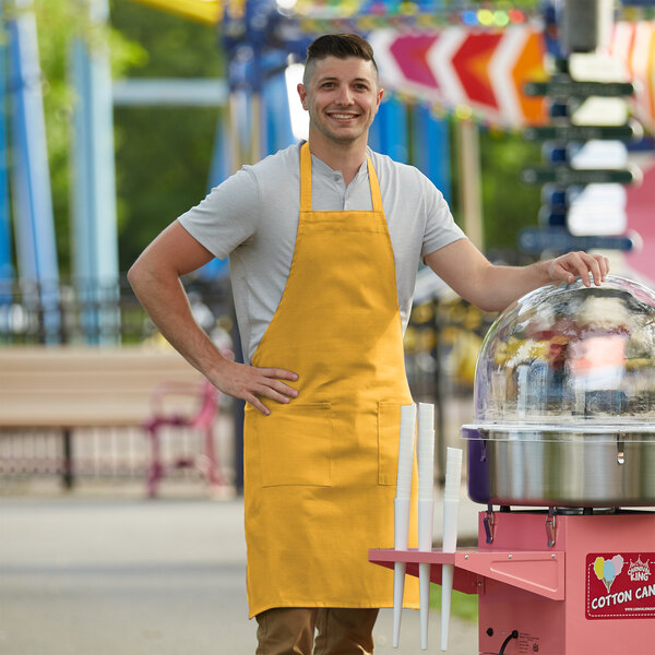 A man wearing a Choice yellow poly-cotton bib apron standing next to a cotton candy machine.