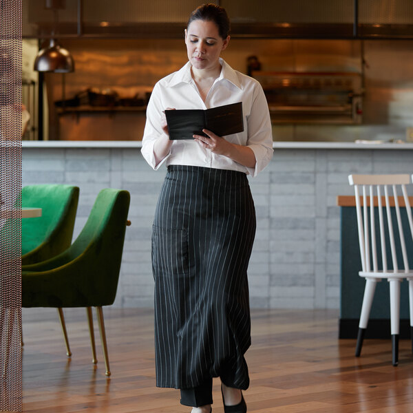 A woman wearing a black and white pinstripe bistro apron with a pocket in a restaurant.