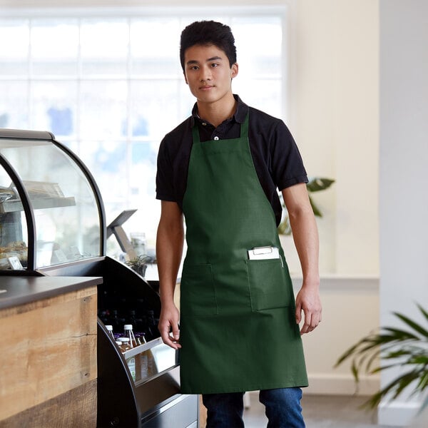 A man wearing a Choice hunter green bib apron standing in front of a counter.