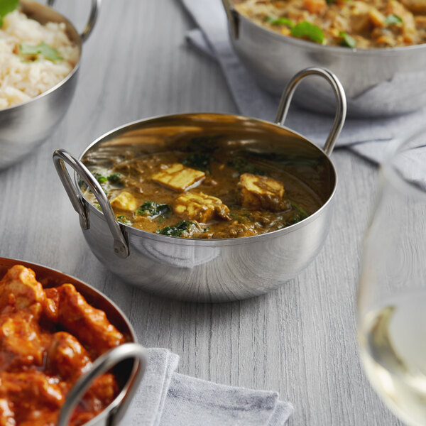 A group of Vollrath stainless steel balti dishes filled with food on a table.