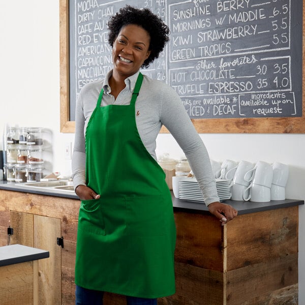 A woman wearing a Choice Kelly Green bib apron standing in front of a counter.