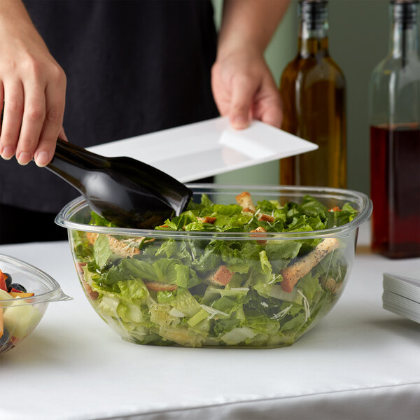 A person pouring salad into a Fineline clear plastic bowl.