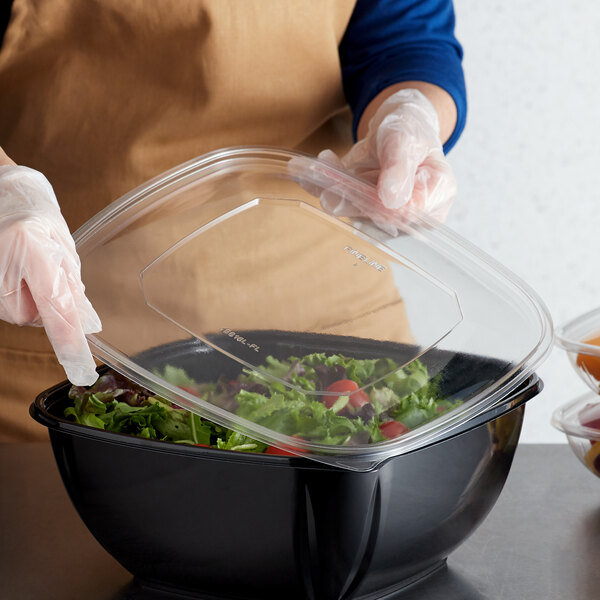 A person holding a Fineline clear plastic lid over a salad in a plastic container.