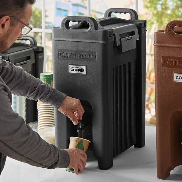 A man pouring coffee from a CaterGator black insulated beverage dispenser into a paper cup.