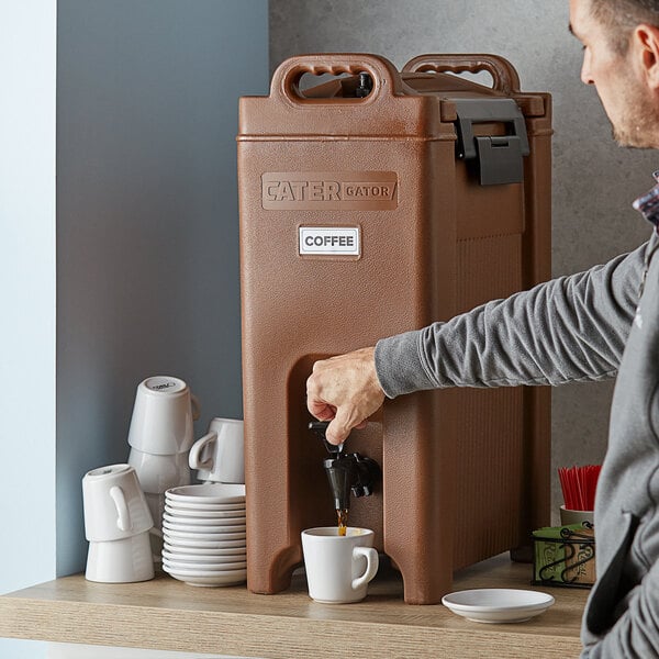 A man using a CaterGator brown insulated beverage dispenser to fill a white mug with coffee.