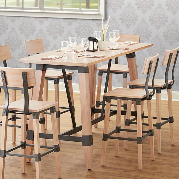 A Lancaster Table & Seating wooden bar height trestle table base with chairs and glasses on it.