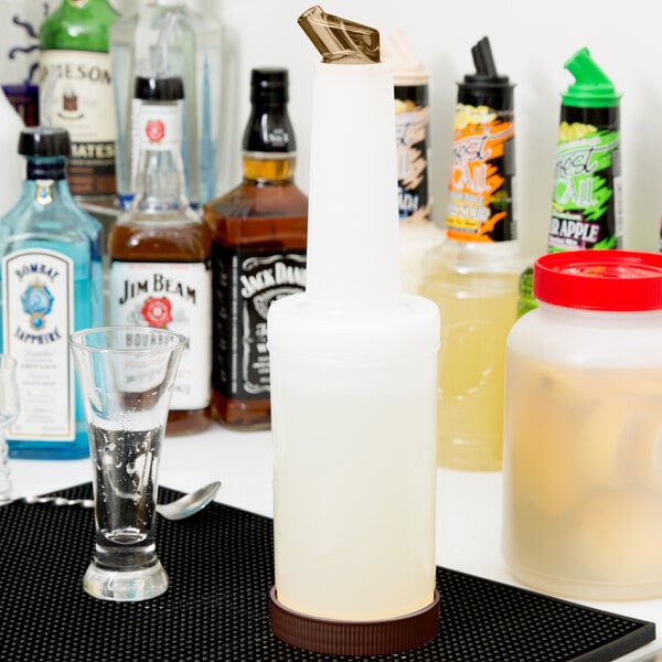 A white Carlisle Store 'N Pour bottle with brown spout and cap on a counter next to other bottles.