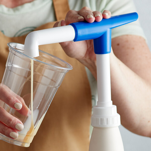 A hand using a blue and white Torani Beverage Base Pump to pour milk into a glass.