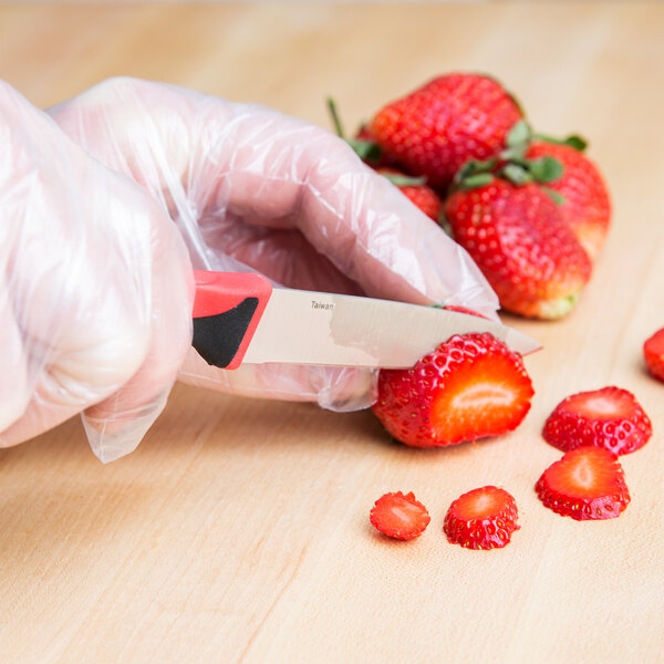 A person in gloves using a Mercer Culinary Millennia Colors paring knife to cut strawberries.