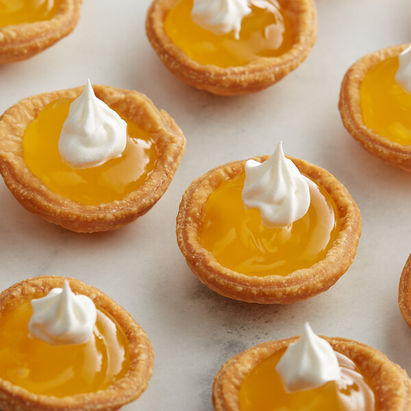 A group of small pies with yellow lemon filling and whipped cream.