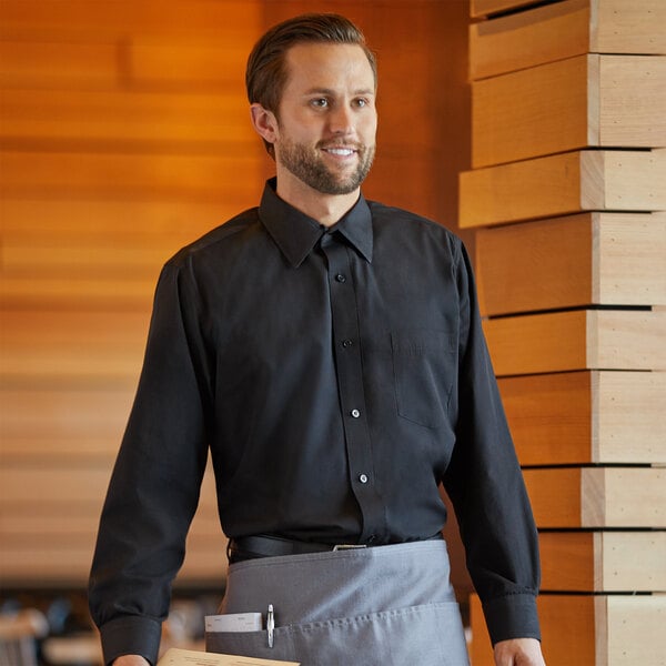 A man in a Henry Segal black dress shirt and apron holding a wooden board on a counter.
