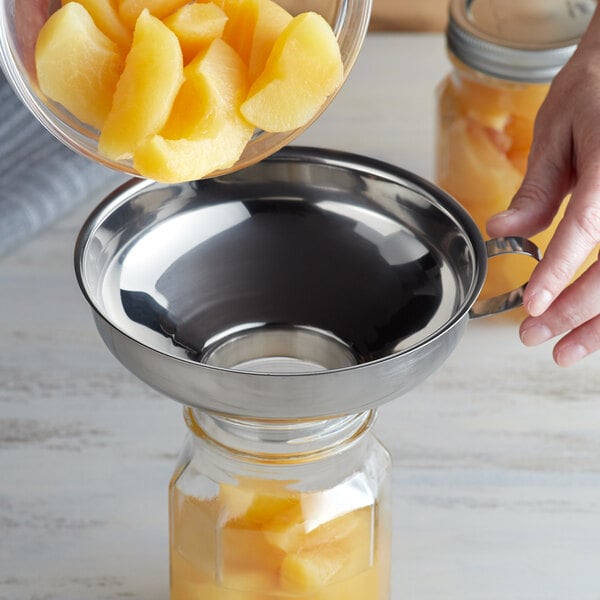 A person using a Fox Run stainless steel canning funnel to pour fruit into a glass jar.