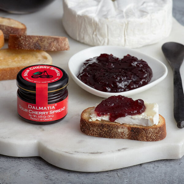 A plate of bread with Dalmatia Sour Cherry Spread and a spoon on a marble board.