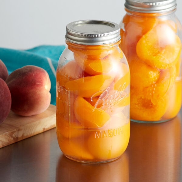Two Ball quart glass canning jars filled with peaches on a table.