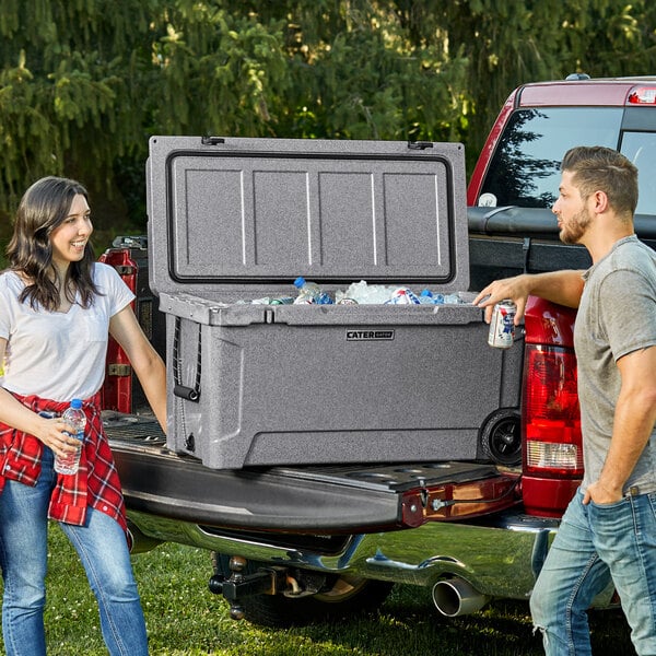 A man and woman standing next to a CaterGator outdoor cooler in the back of a truck.