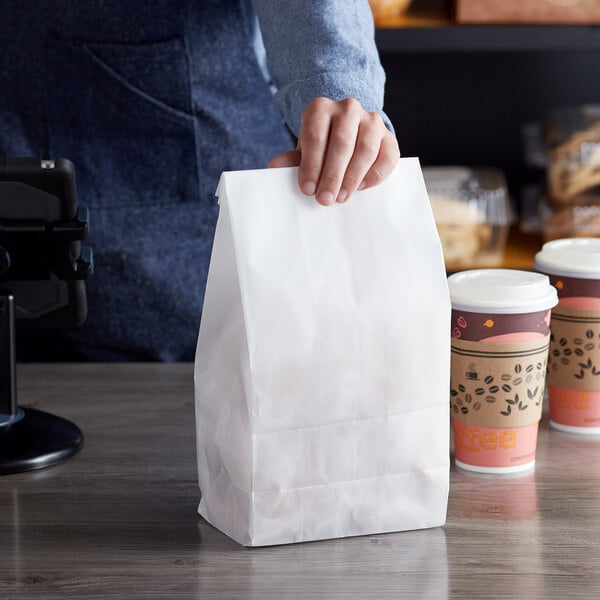 A person holding a Bagcraft white paper bag with coffee cups inside.