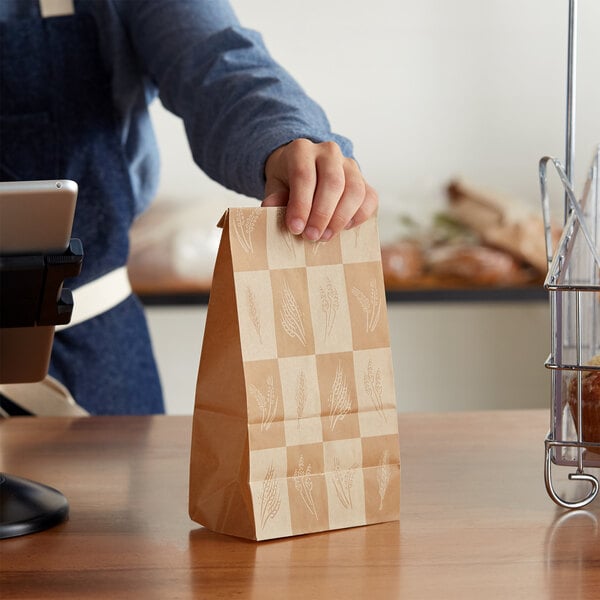 A person holding a Bagcraft Packaging EcoCraft paper bag with a wheat design
