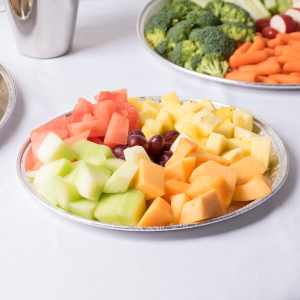 A Durable Packaging round foil catering tray of fruit and vegetables on a table.