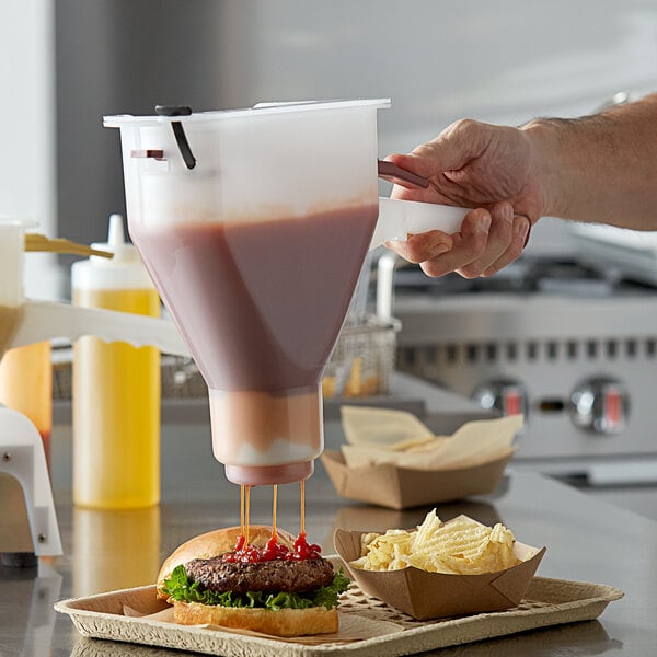 A hand using a Prince Castle ketchup dispenser to pour ketchup onto a burger.