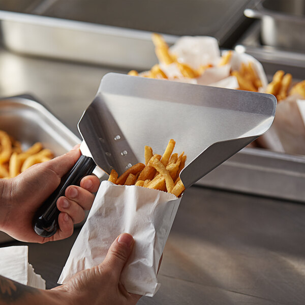 A person using a Prince Castle aluminum French fry bagging scoop to put french fries into a paper bag.