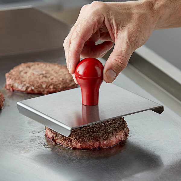 A person using a Prince Castle meat press to stamp a meat patty on a griddle.