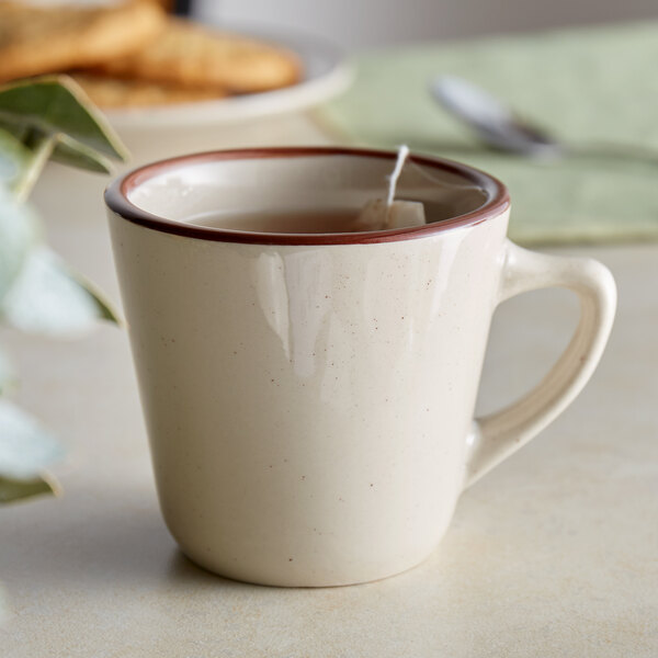An Acopa brown speckle stoneware coffee cup filled with tea on a saucer with cookies.