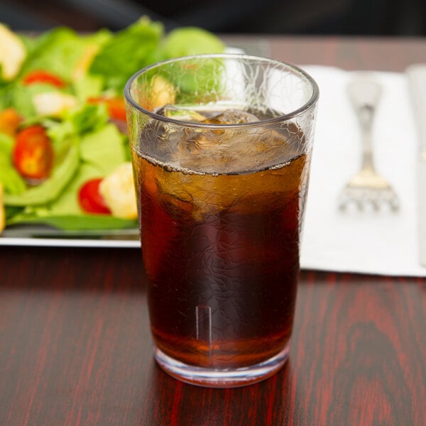 A clear plastic tumbler of ice tea with ice in front of a salad