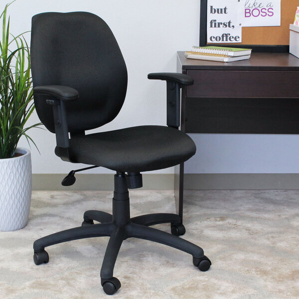 A black Boss mid-back office chair with adjustable arms in front of a desk.