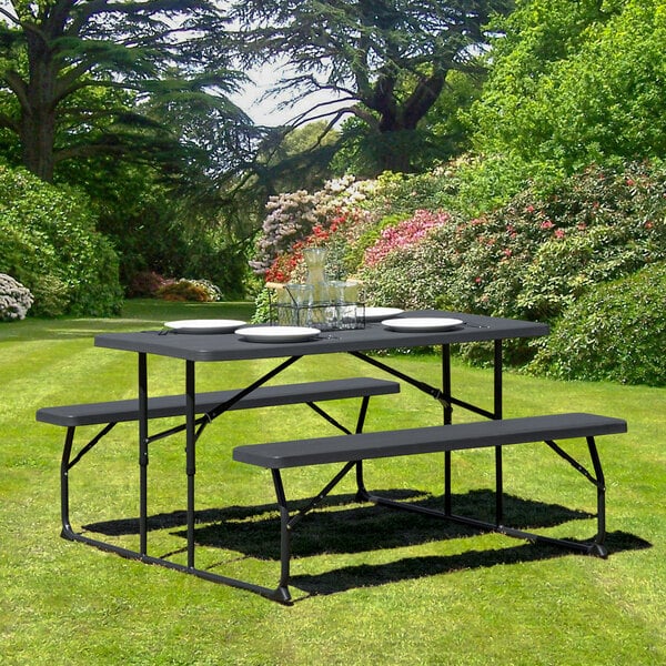 A Flash Furniture charcoal plastic folding table with 2 benches set up in a park.