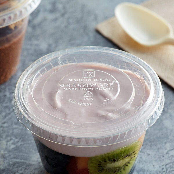 A plastic container with a Fabri-Kal Greenware compostable lid and yogurt with a spoon.