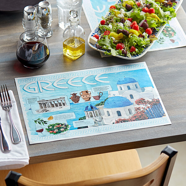 A table set with Greek themed paper placemats with a salad on a plate.
