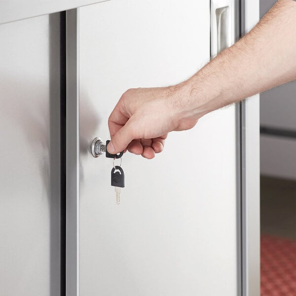 A hand using a key to open a cabinet door on a Regency stainless steel table.