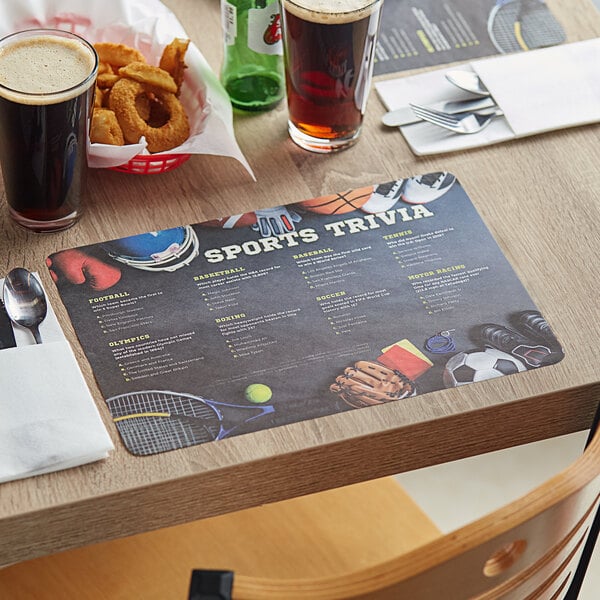 A table with Choice Sports Trivia paper placemats, food, and drinks on it.