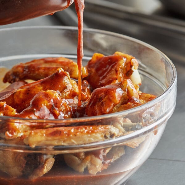 A bowl of chicken wings being poured with Sweet Baby Ray's Jamaican Jerk Wing Sauce.