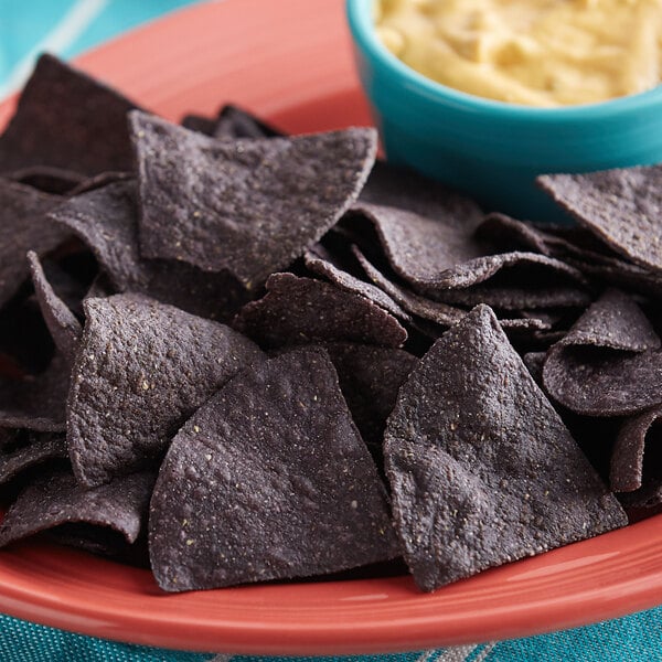 A plate of Mission blue triangle corn tortilla chips with a bowl of dip.