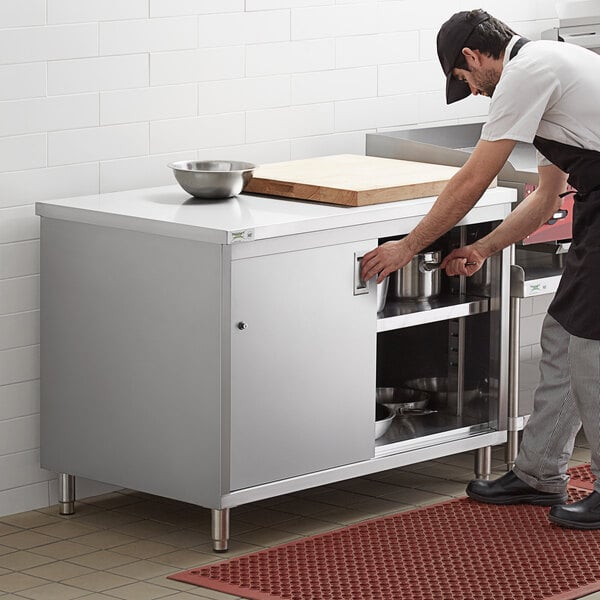 A man in a black apron opening a Regency stainless steel table with sliding doors.